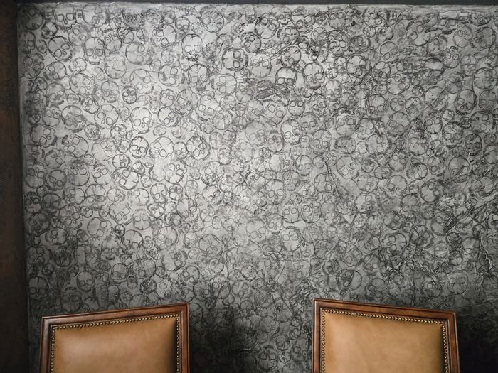 Silver and charcoal stamped skull relief plaster wall behind leather nailhead chairs